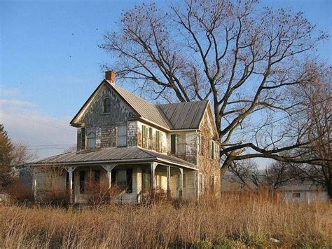 An Old House Sitting In The Middle Of A Field With Tall Grass And Bare