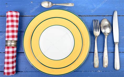 Colorées et fleuries façon quimper, couple de bretons avec le traditionnel liseré bleu moucheté. Assiette avec couverts argentés sur une vieille table ...