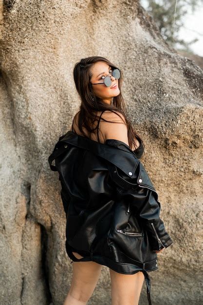 Модная чувственная женщина в черной кожаной куртке и стильных солнцезащитных очках позирует над