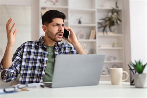 Confused Arab Man Talking On Mobile Phone Using Laptop Stock Photo