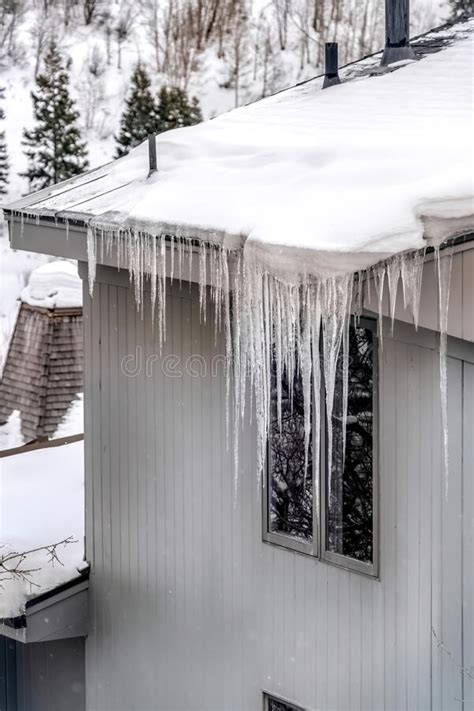 Sharp Spiked Icicles On Roof With Snow Against Snowy Hill Landscape In