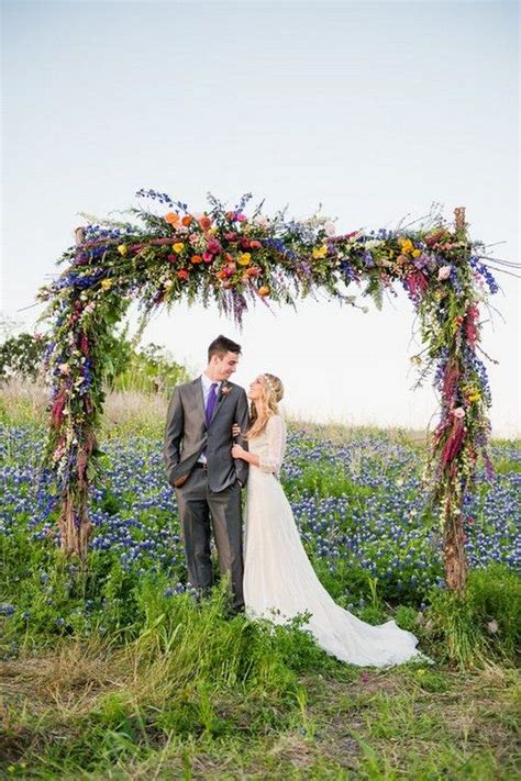 A Bride And Groom Standing Under An Arch Made Out Of Flowers In The