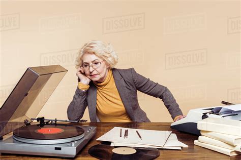 Upset Senior Woman Listening Vinyl Record Player At Table Stock Photo