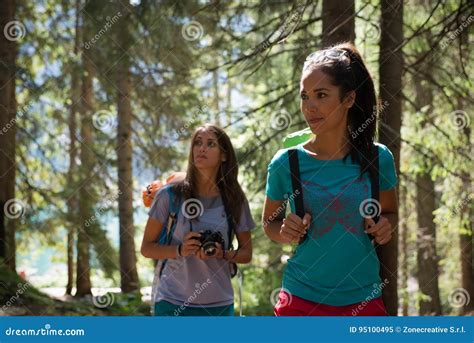 Two Women Walking Along Hiking Trail Path In Forest Woods During Sunny