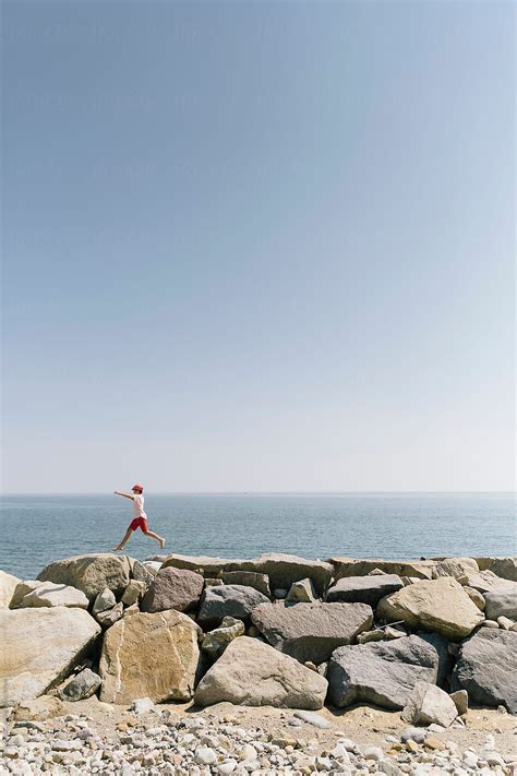Barefoot Summer Lifestyle With Boy Walking On And Jumps On Sea Wall By
