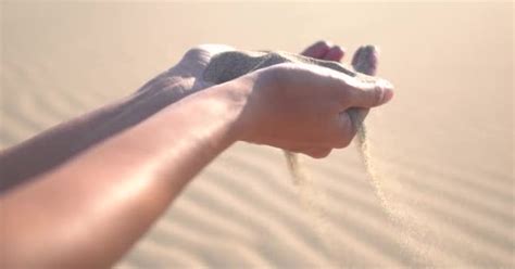 close up of woman pouring sand running through fingers slow motion at the beach with sun flare