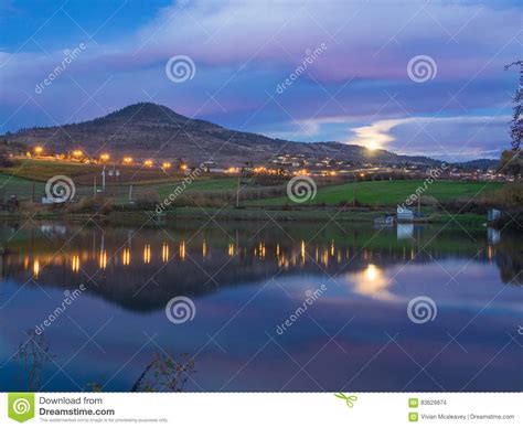 City Lights Rising Moon And Mountain Reflected In Pond Stock Photo