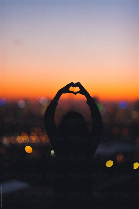 Woman In Silhouette Making Heart Shape With Hands On Sunset By