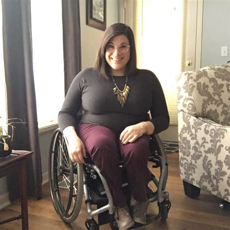 A Woman Sitting In A Wheel Chair Smiling At The Camera While Holding