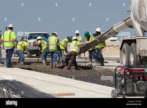 Team Of Male Highway Construction Workers Pour Fresh Concrete On Beam