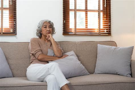 thoughtful mature woman sitting on couch at home alone dreaming and planning serious pensive