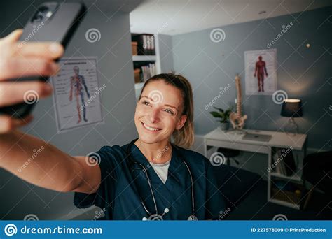 Caucasian Female Nurse Standing In Doctors Office Taking Selfie On Cellular Device Stock Image