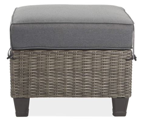 An Ottoman With Grey Cushions And Wicker On The Bottom In Front Of A
