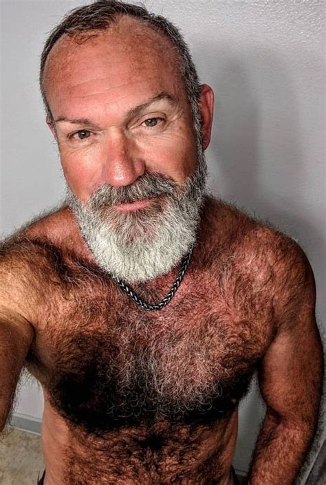 An Older Man With A Beard And No Shirt On Posing In Front Of A White Wall