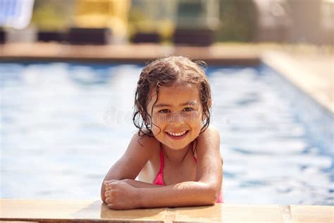 Portrait Of Young Girl Leaning On Edge Of Swimming Pool On Summer