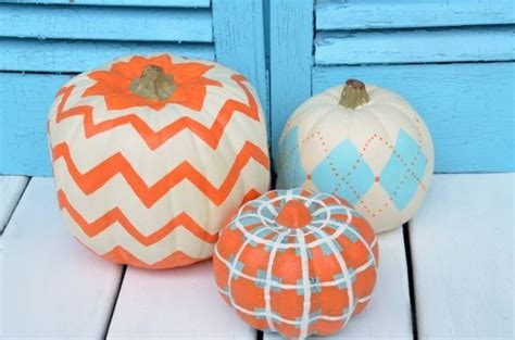Three Painted Pumpkins Sitting Next To Each Other On A White Wooden