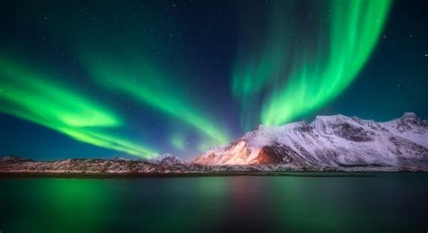 ロフォーテン諸島ノルウェーのオーロラとビーチ 美しいオーロラ 極光と星空 空の反射と街の明かり雪山とオーロラ海の夜の冬の風景 プレミアム写真