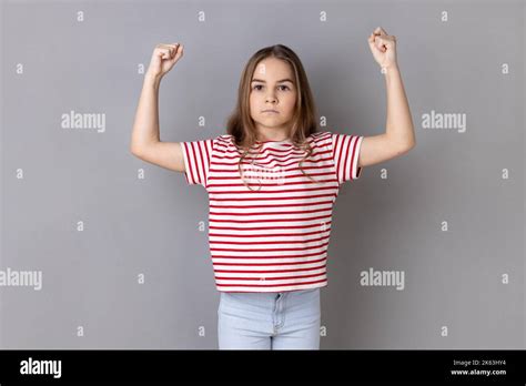 Ein Starkes Dunkelhaariges Kleines Mädchen Das Gestreiftes T Shirt Trägt Und Die Arme Hebt