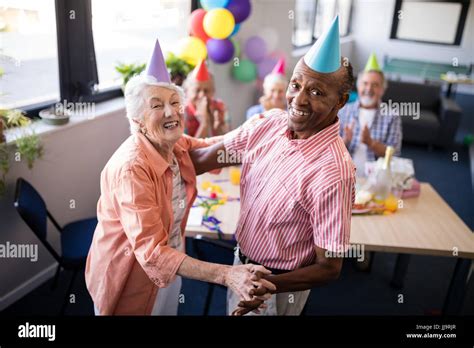 Portrait Of Happy Senior Couple Dancing By Table At Birthday Party