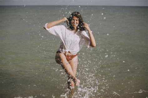 Mujer Joven Feliz En Camisa Blanca Mojada Salpicando Gotas De Agua Con La Pierna En El Mar Chica