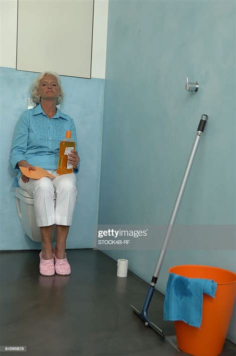 Senior Woman Next To Cleaning Utensils Sitting On A Toilet Photo