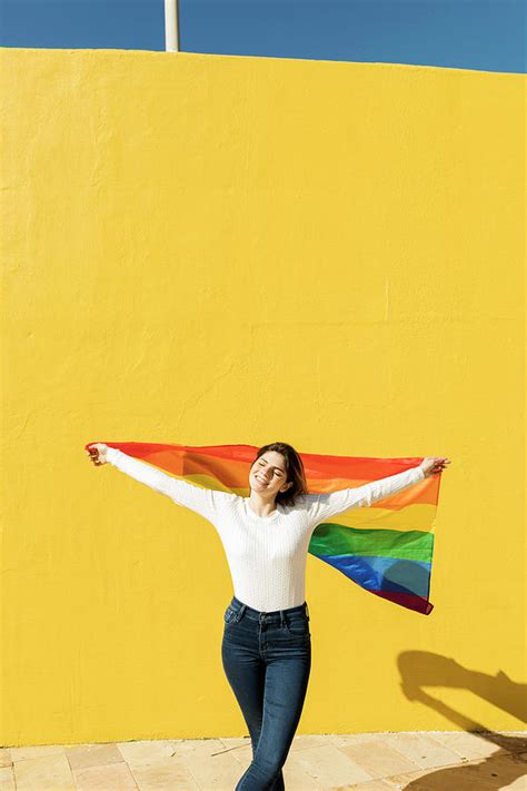 lesbian woman with rainbow flag in front of yellow wall photograph by cavan images fine art