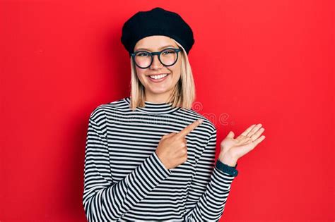 beautiful blonde woman wearing french look with beret an glasses amazed and smiling to the