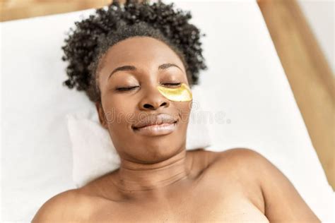 African American Woman Lying On Massage Table Having Eye Mask Treatment At Beauty Salon Stock