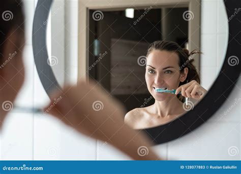 Young Brunette Woman Brushing Her Teeth In Front Of Bathroom Mirror