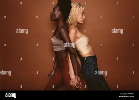 Two Women Standing With Backs Against Each Other Side View Studio Shot Of Diverse Females