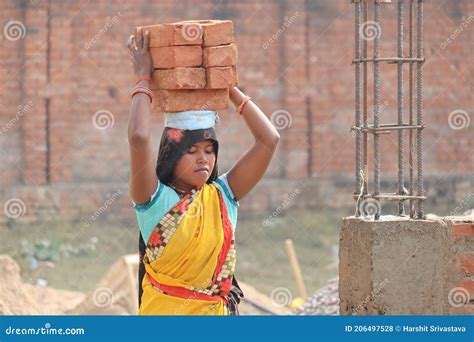 A Poor Female Construction Worker Carrying Heavy Bricks On Her Head
