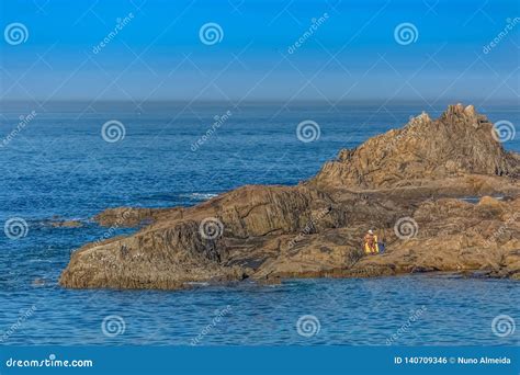 View Of Man Sitting On The Rocks Reading The Newspaper And Sunbathing On Yellow Towel Ocean And