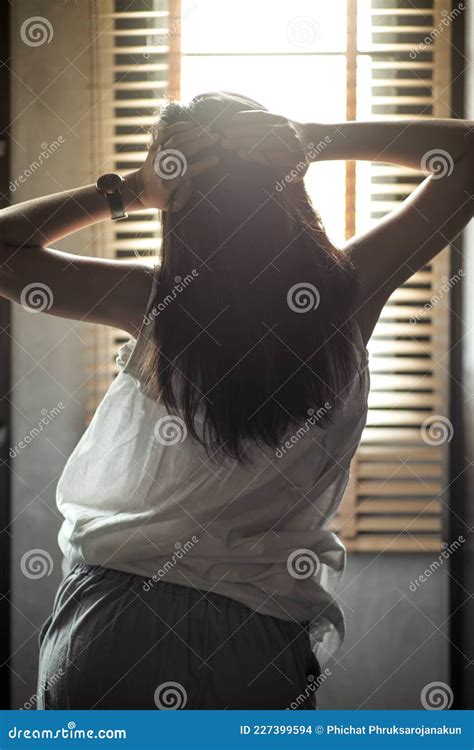 back portrait of girl puts her hands on the head with sunlight and blurred curtain in background