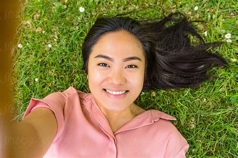 Young Filipino Woman Taking A Selfie While Lying Down On Grass Del Colaborador De Stocksy