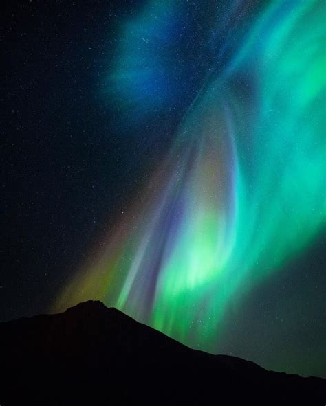 An Aurora Bore Is Seen In The Night Sky Over Mountains And Snow Capped