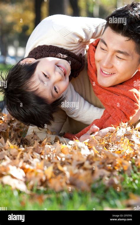 Father And Son Lying On The Grass Surrounded By Autumn Leaves Having