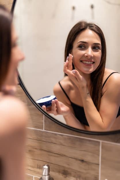 Mujer Joven Mirando Al Espejo En Casa Y Aplicando Crema En La Cara En El Ba O Foto Premium