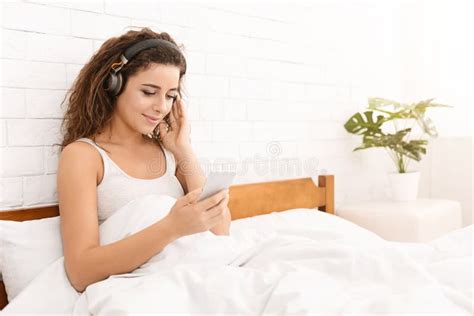 Girl Listening To Music With Wireless Headphones In Bed Stock Photo