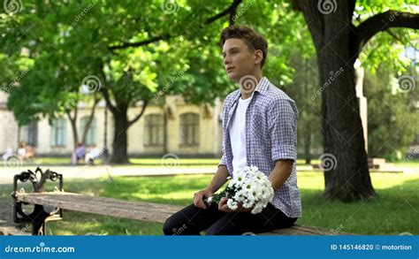 Teenager With Bouquet Of Flowers Sits On Bench In Park Waiting For