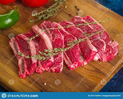 Raw Meat Steaks With Fragrant Rosemary Sprigs On A Wooden Cutting Board
