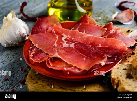 closeup of an earthenware with some slices of spanish serrano ham on a wooden chopping board