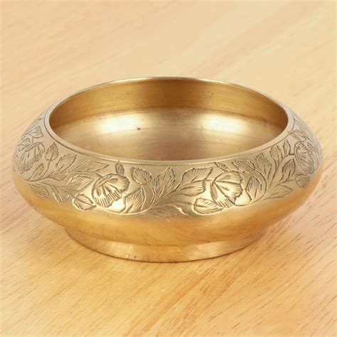 A Gold Colored Metal Bowl Sitting On Top Of A Wooden Table Next To A