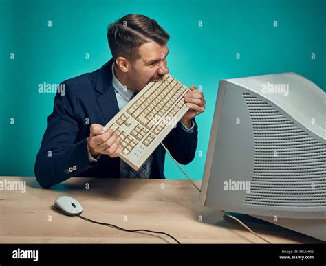 Angry Businessman Breaking Keyboard Against Blue Background Stock Photo