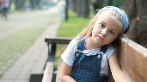 Little Serious Child Girl Sitting Alone On A Bench In Summer Park Stock