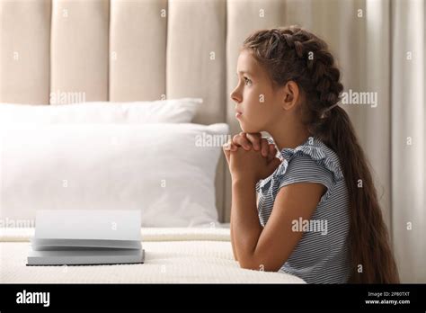 Cute Little Girl Praying Over Bible In Bedroom Space For Text Stock