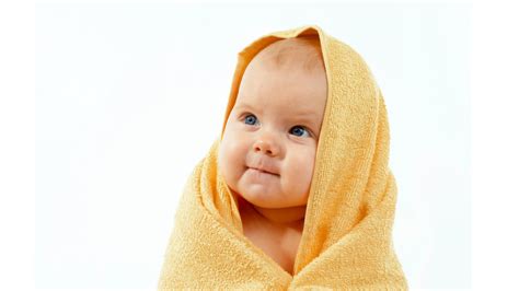 Cute Smiling Baby Sitting On Floor Covered With Yellow Towel In White