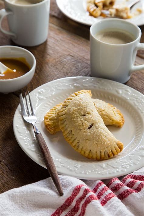 Two Pastries On A White Plate With Silverware And Cups Of Coffee In The
