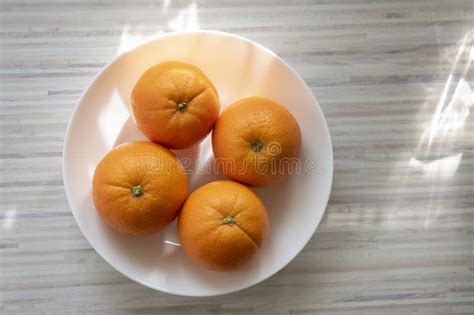 Group Of Four Orange Oranges On Unpee On White Plate On The Table In