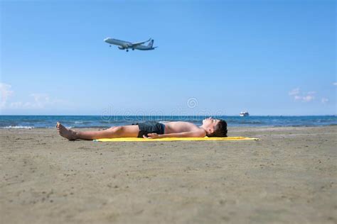 Teen Boy Lies On Yellow Towel And Sunbathes On The Beach On The Sea And