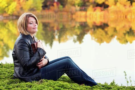 mature christian woman embracing her bible in a city park beside a lake in autumn edmonton